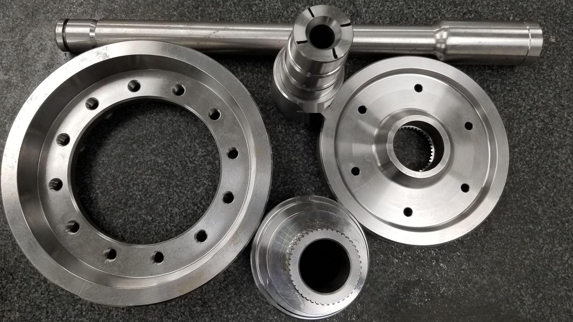 Machined powertrain components: a long shaft, a large bolt-circle ring, a splined flange, a splined hub and a slotted sleeve